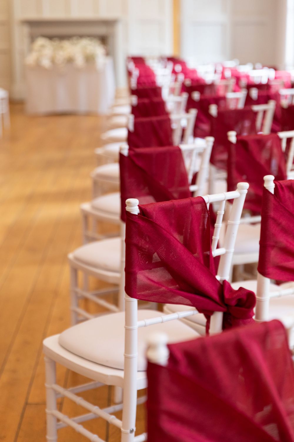 White chiavari chairs with deep red satin sashes arranged in rows for an elegant wedding ceremony setup.