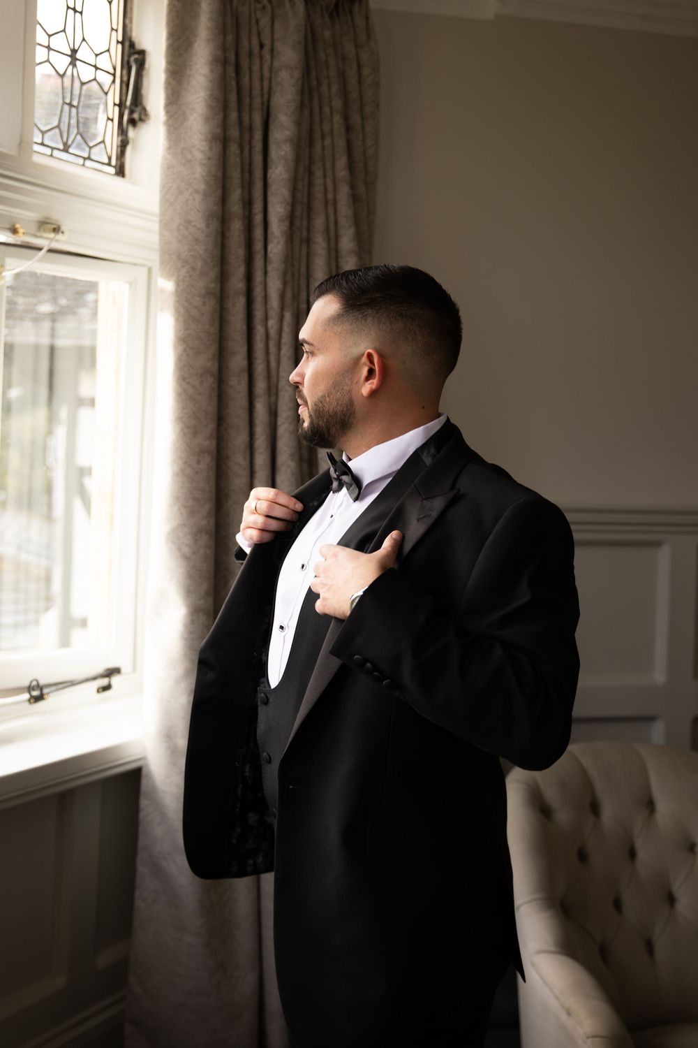 Series of photos showing a groom adjusting his bowtie while getting ready in a well-lit room.