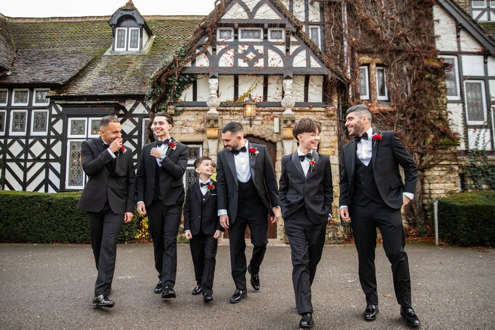 Wedding party walking together outside a traditional Tudor-style building in formal attire.