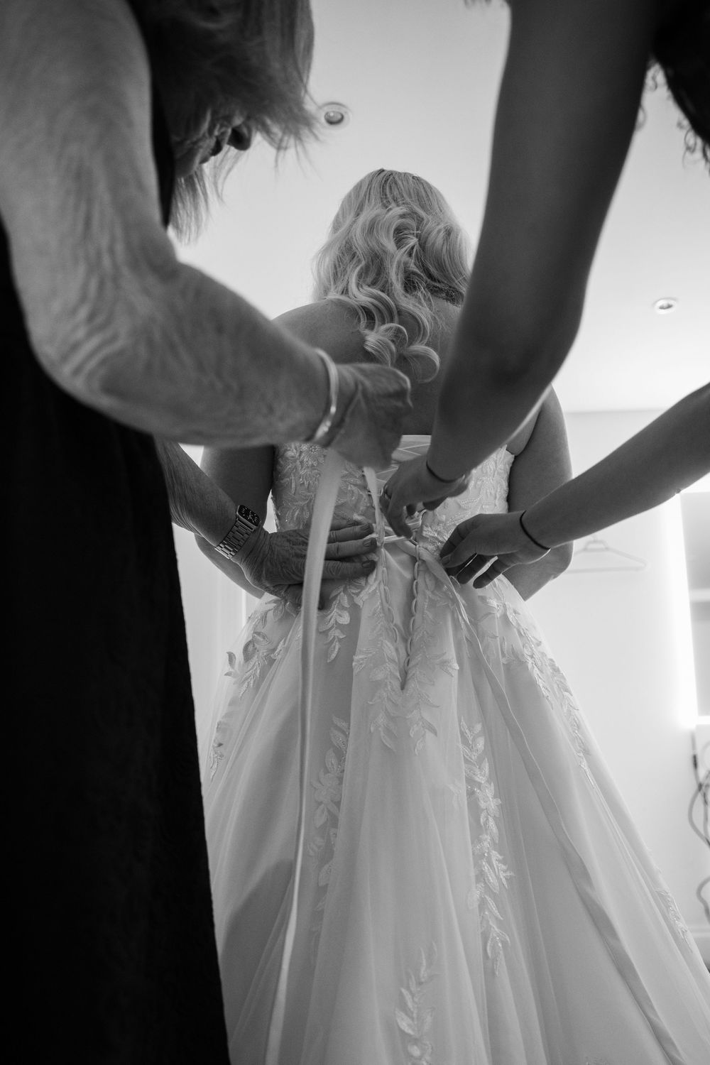 Close-up shots of hands lacing up the back of an elegant white wedding dress with delicate details.