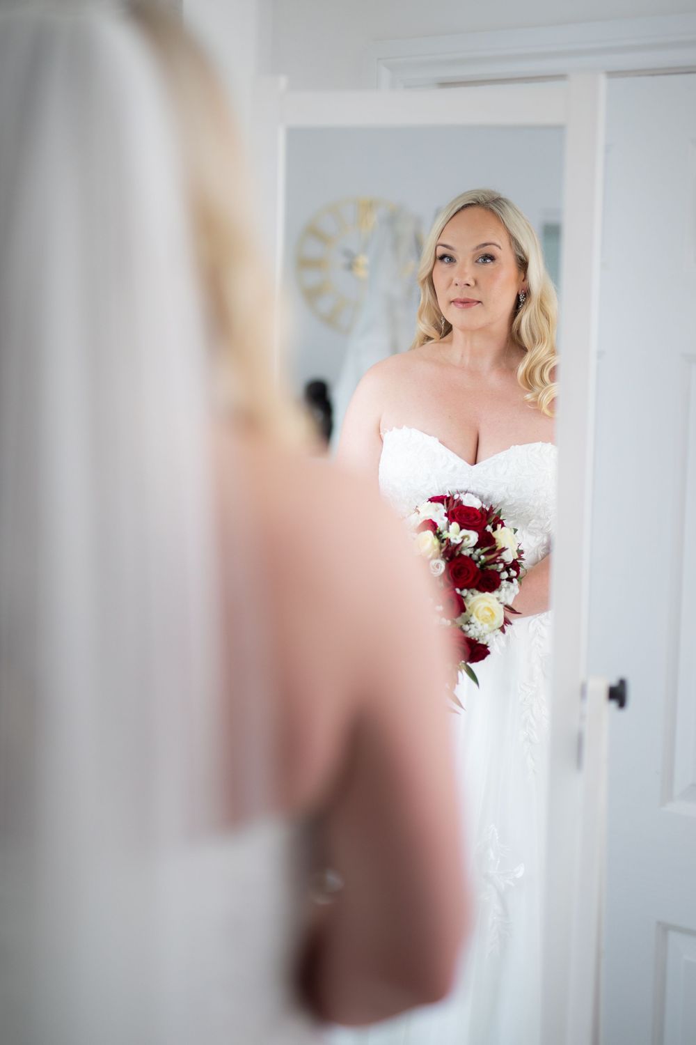 Elegant bridal portrait in soft natural light showing off white wedding gown and red rose bouquet.