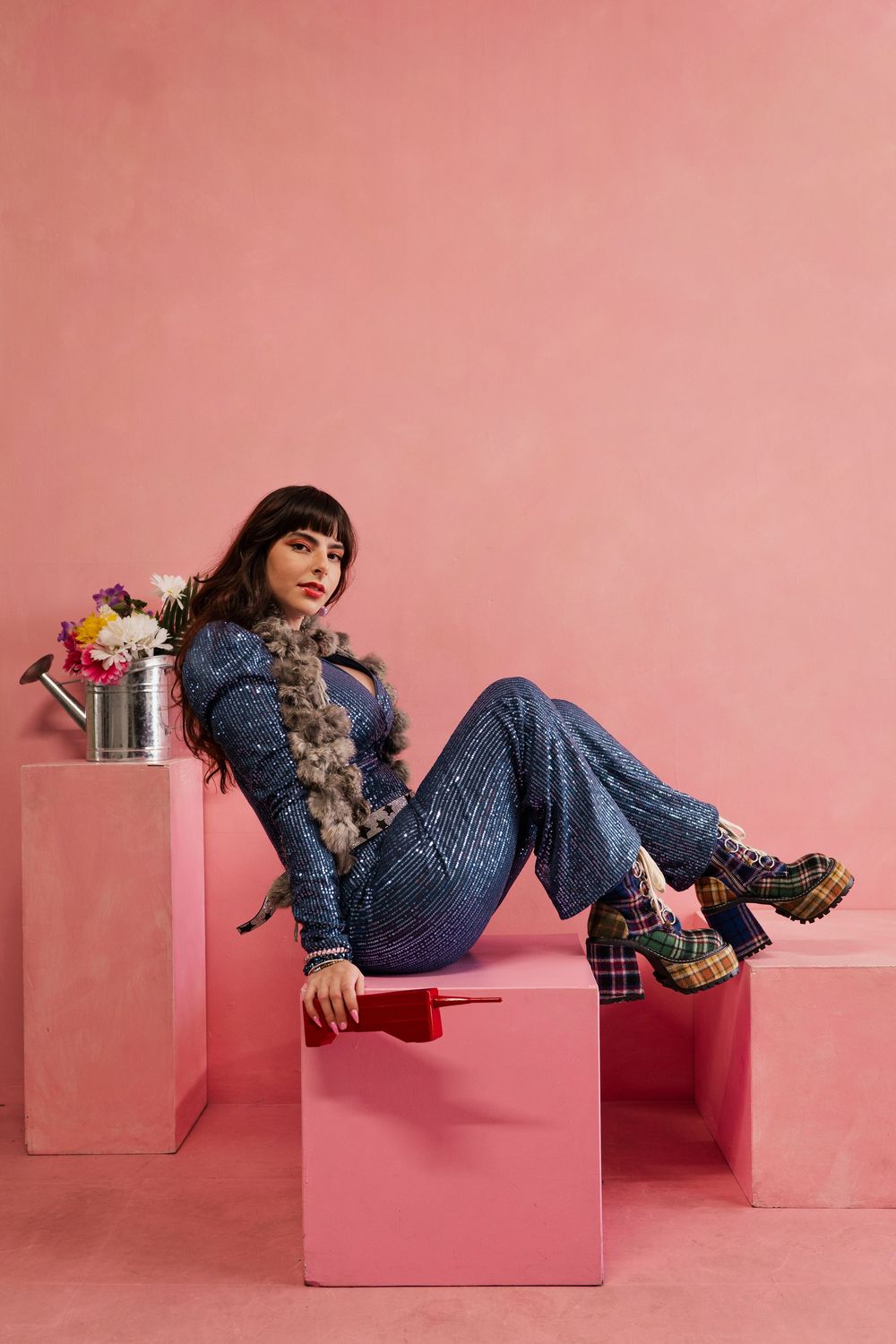 A person in denim outfit lounges on pink geometric blocks against a pink backdrop in a creative fashion photoshoot.