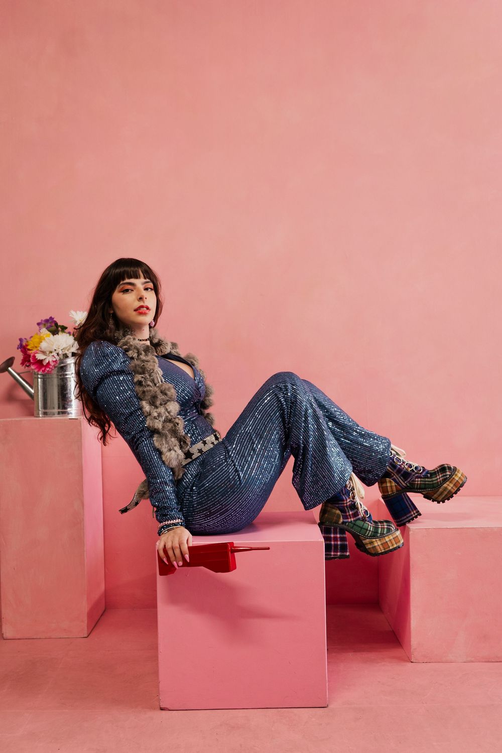 Fashion model in denim outfit lounges on pink geometric blocks in artistic studio photoshoot series.