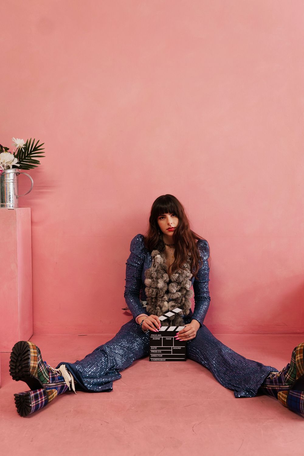 Person in blue denim outfit sits against pink wall holding vintage camera in artistic photo series.