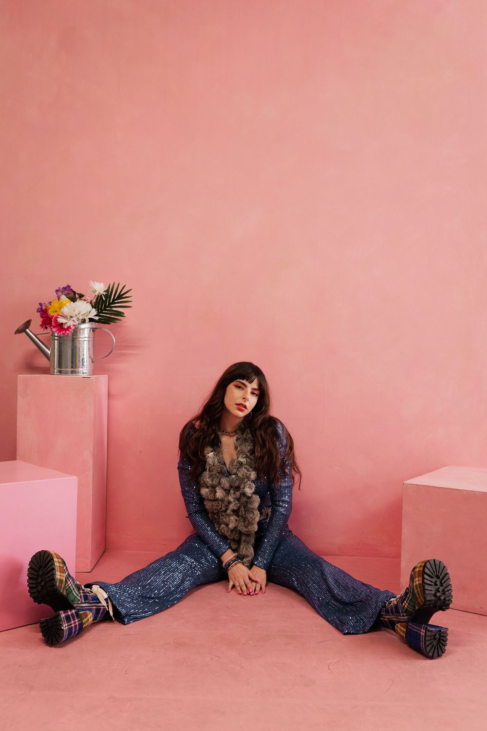 A person in brown floral top and flared jeans poses against a pink wall in a series of artistic shots.