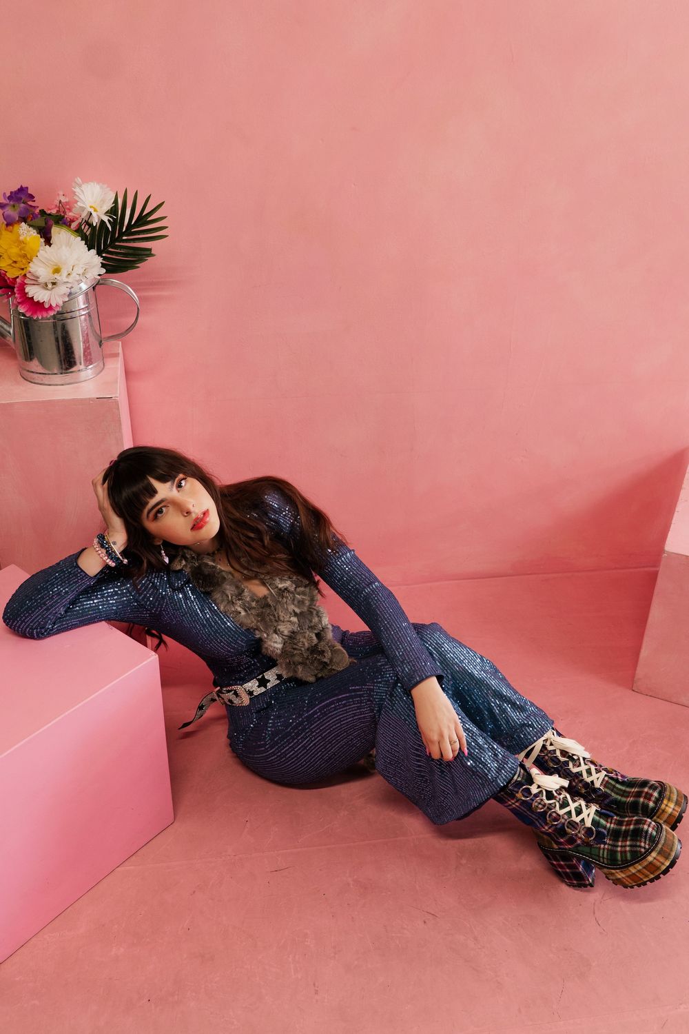 A person in navy blue sweater and plaid skirt lies on pink floor in artistic fashion photography series.