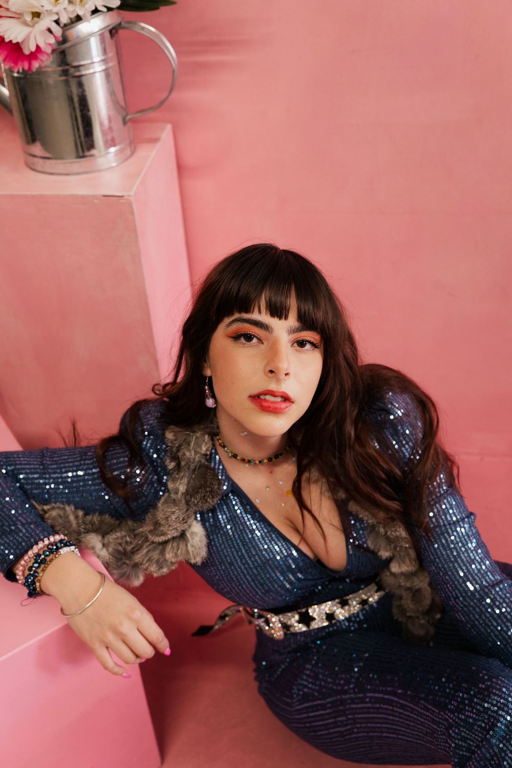 Person in a sparkling navy blue dress poses against a pink background in a glamorous photoshoot series.