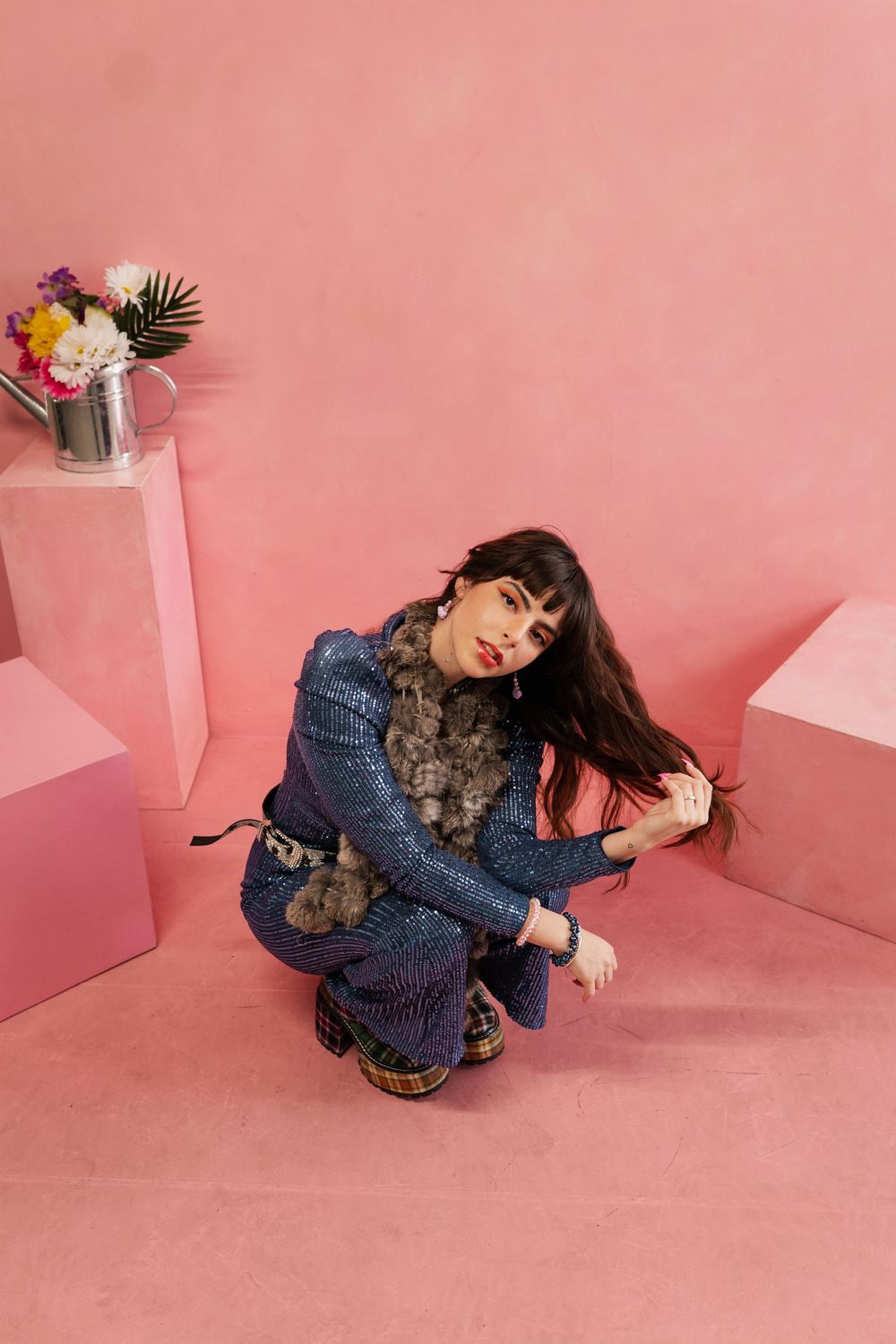 Person in denim outfit reclining on pink floor against pink wall with floral decor.