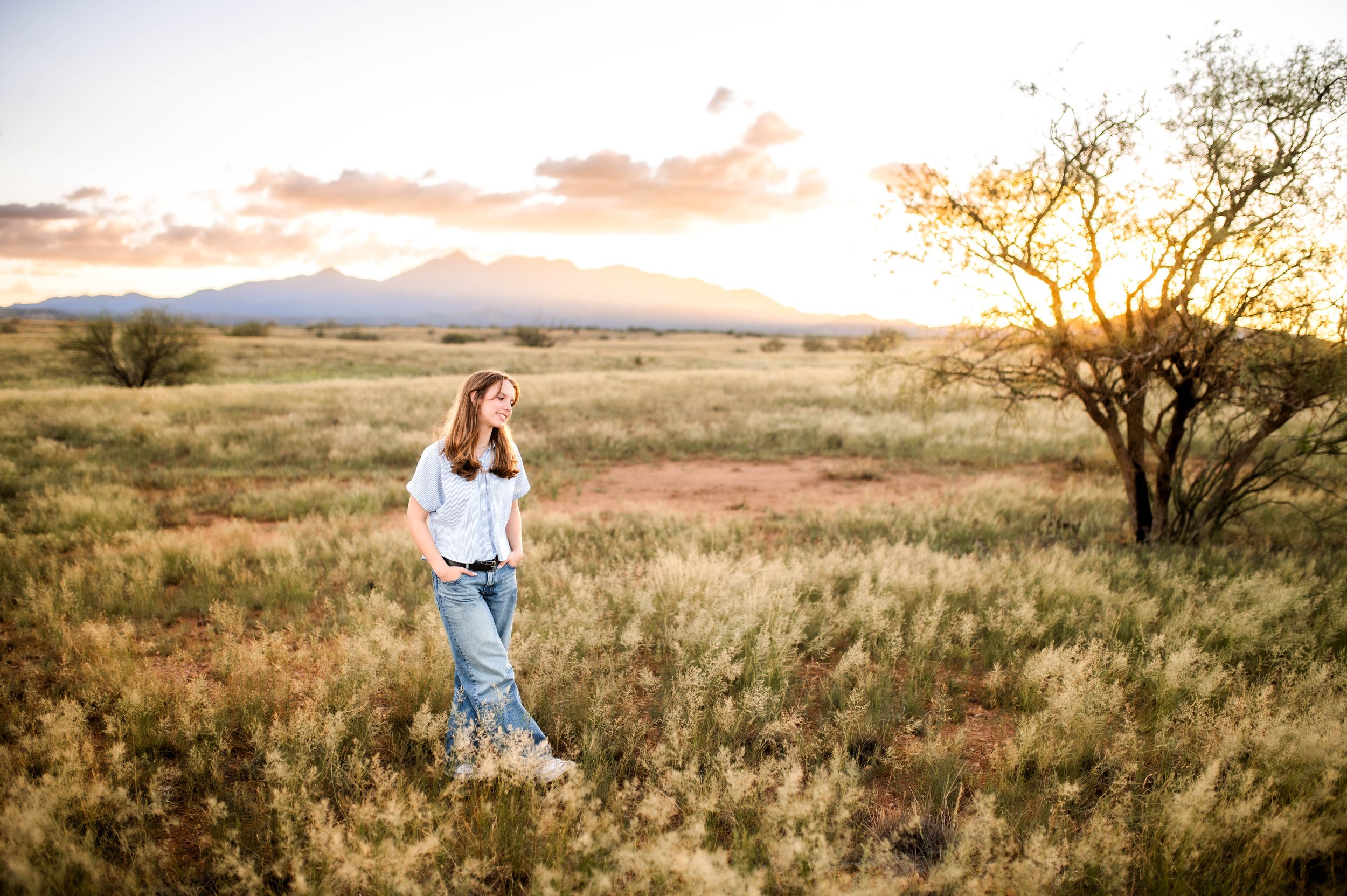 Young woman in white top and jeans walking through scenic desert grassland at golden hour sunset.