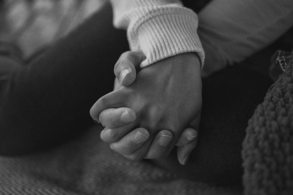 A black and white close-up photo shows hands holding each other in an intimate and caring gesture.