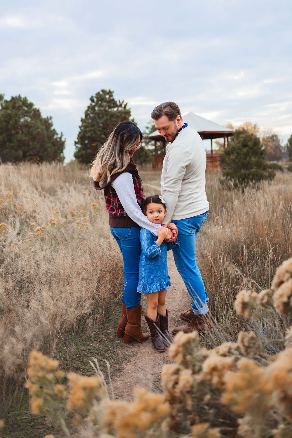 A family shares a tender moment together in a field of dried grass and wildflowers during golden hour.