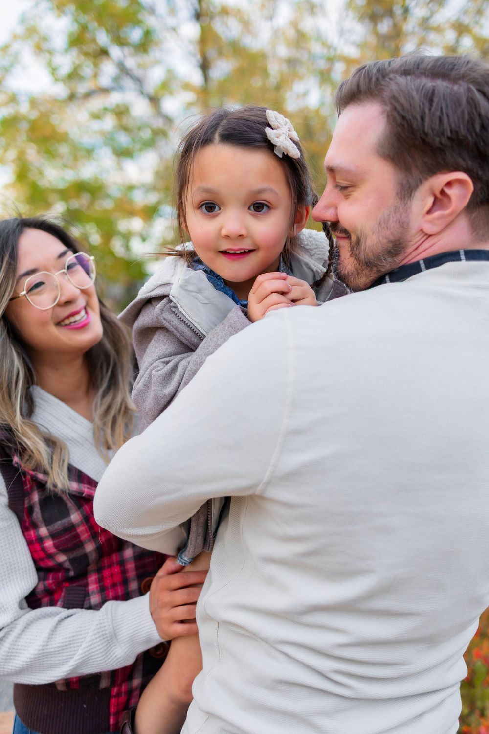A family wearing plaid and white sweaters embraces and plays together in an autumn outdoor setting.