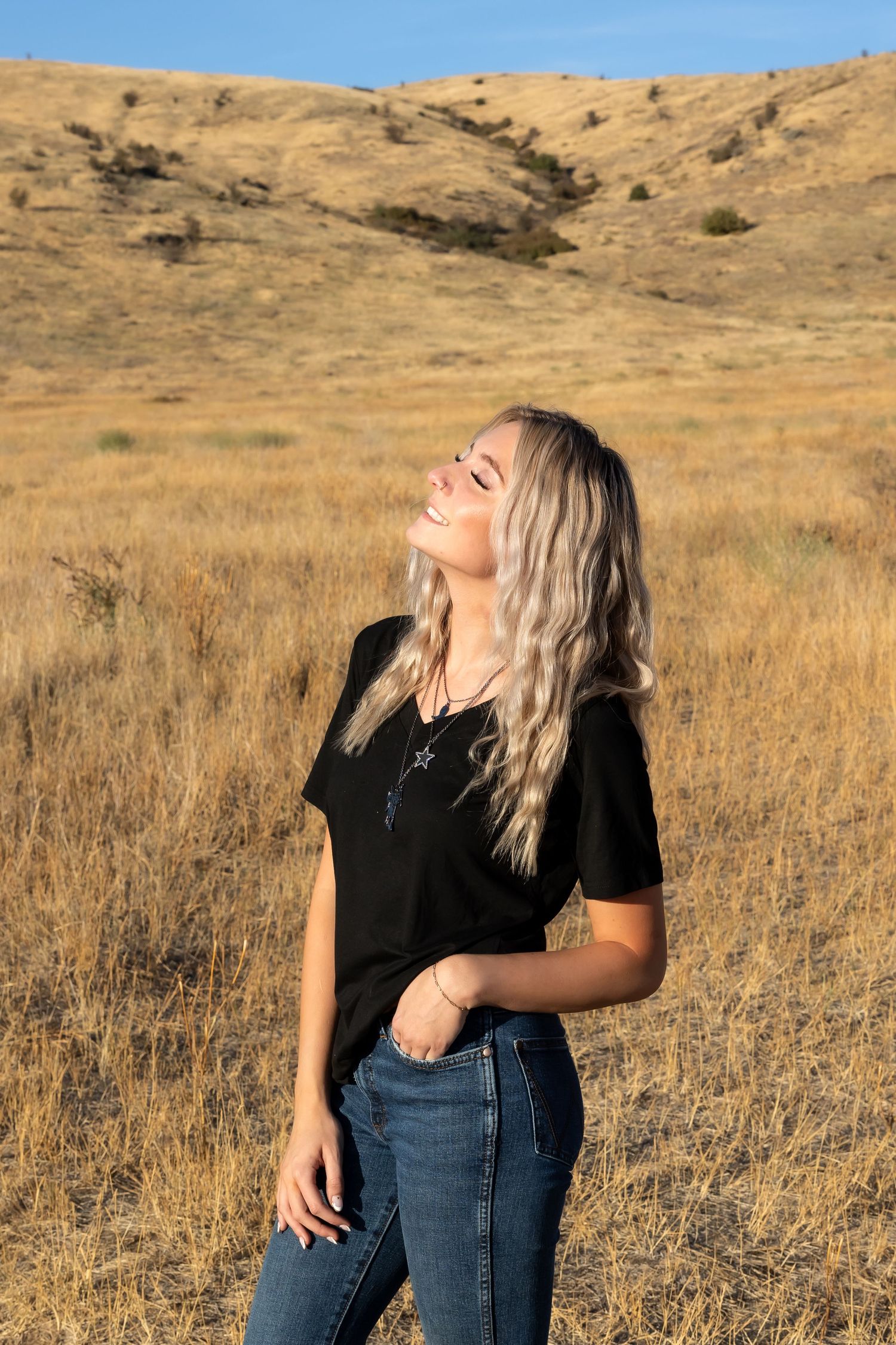 A figure in a black top and jeans poses against a golden hillside backdrop during sunset.
