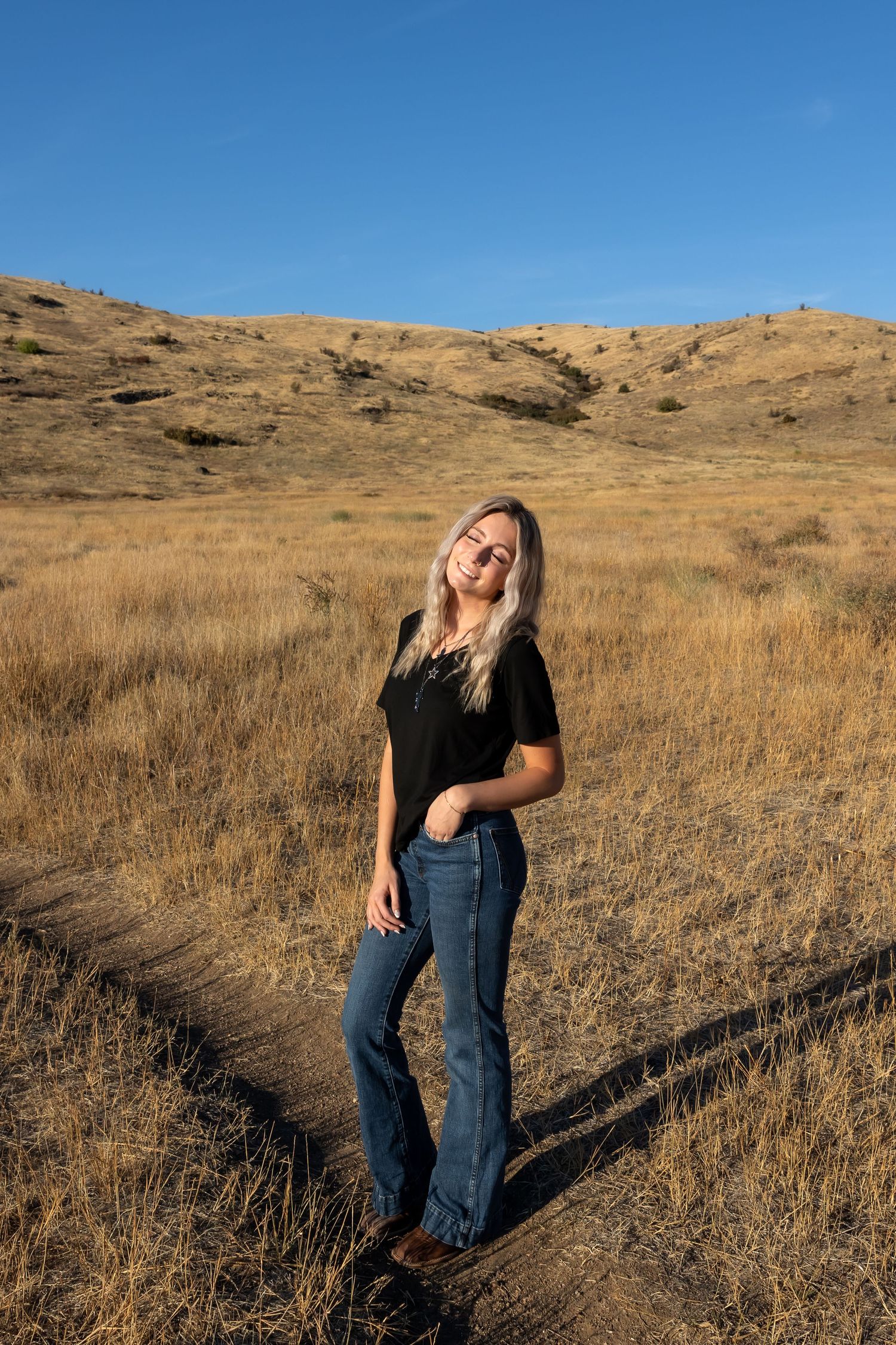Casual outdoor portrait in front of rolling hills with dried grass and bright blue sky.