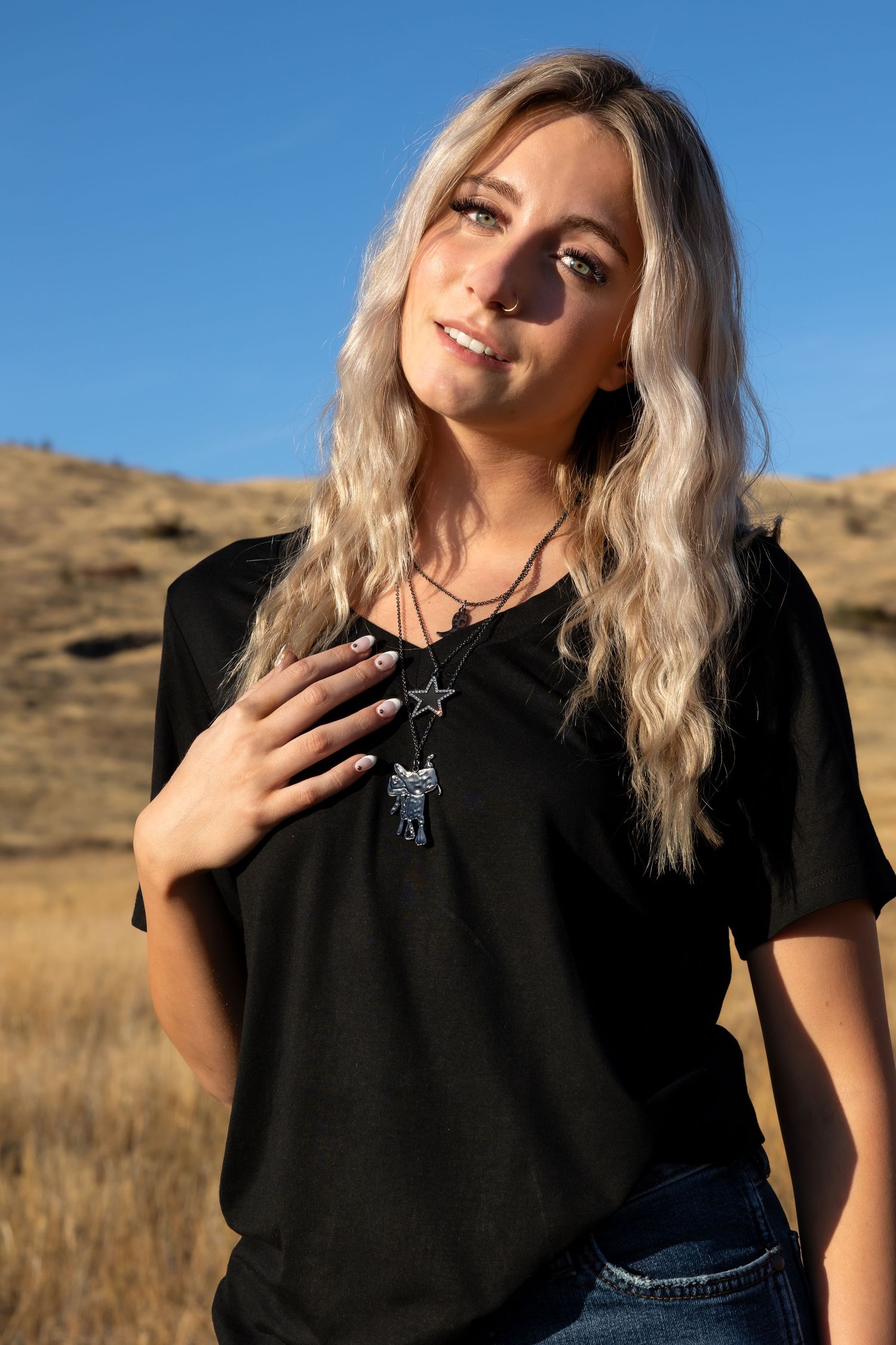 Fashion model poses in black t-shirt and star necklace against golden hillside backdrop in multiple shots.