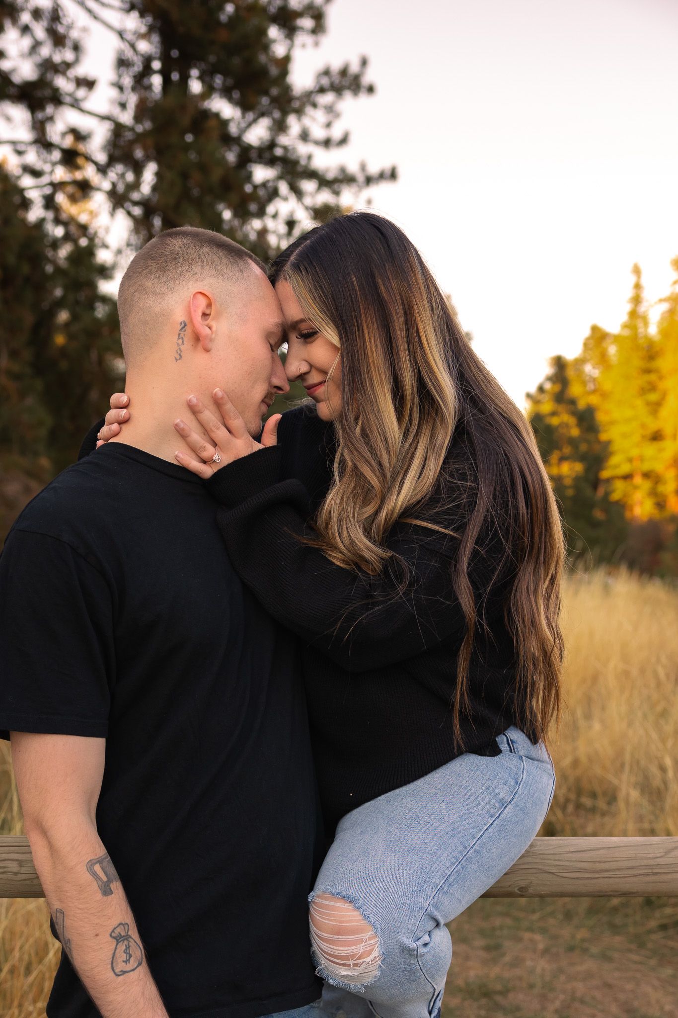 Romantic couple embraces in a golden field at sunset wearing black shirts and jeans.