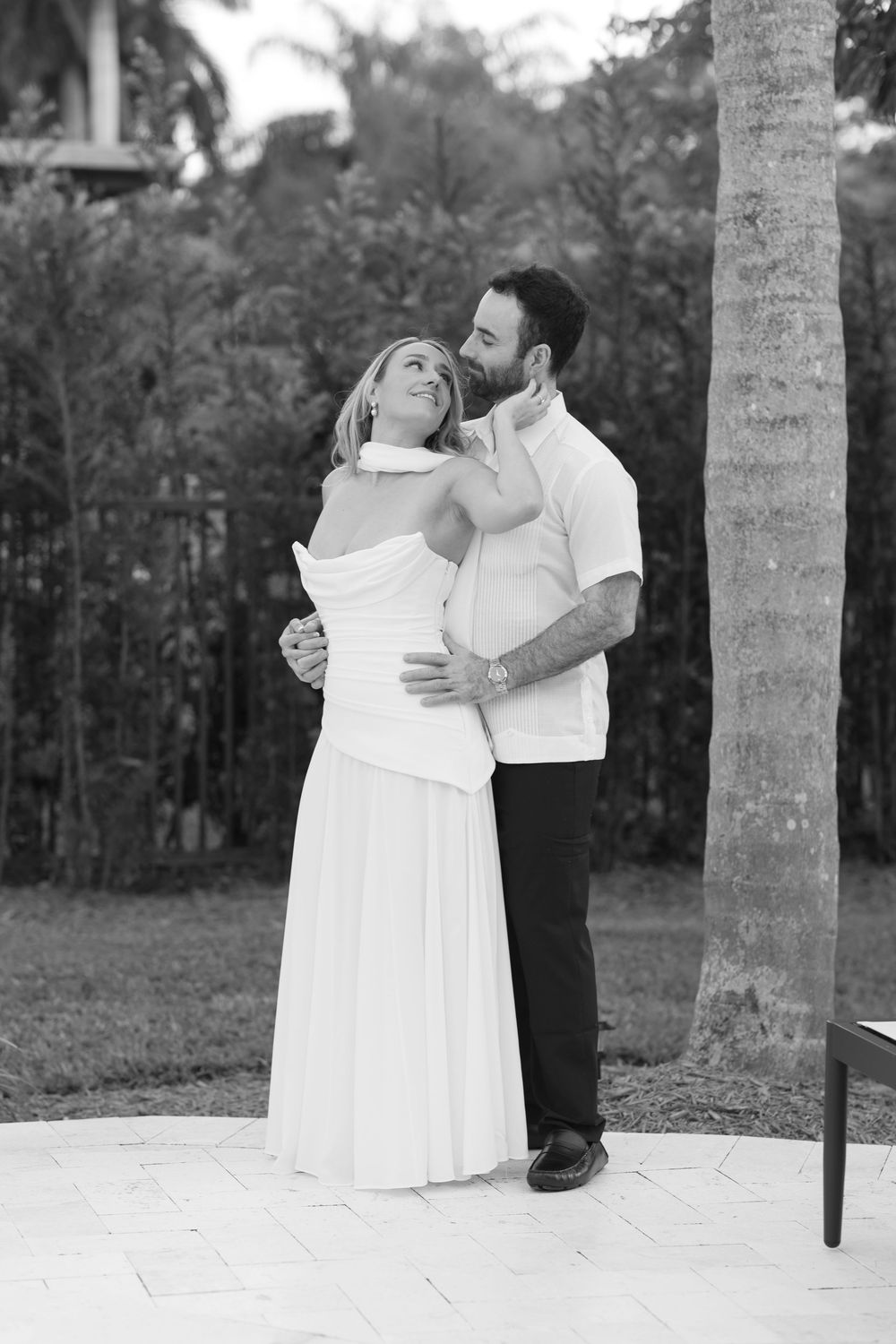 A romantic black and white photo series showing a couple in formal attire embracing among palm trees.