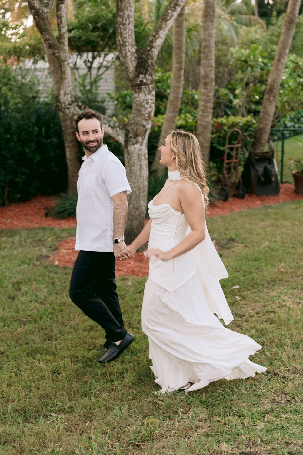 A couple in wedding attire playfully runs through a wooded area during their outdoor photo session.