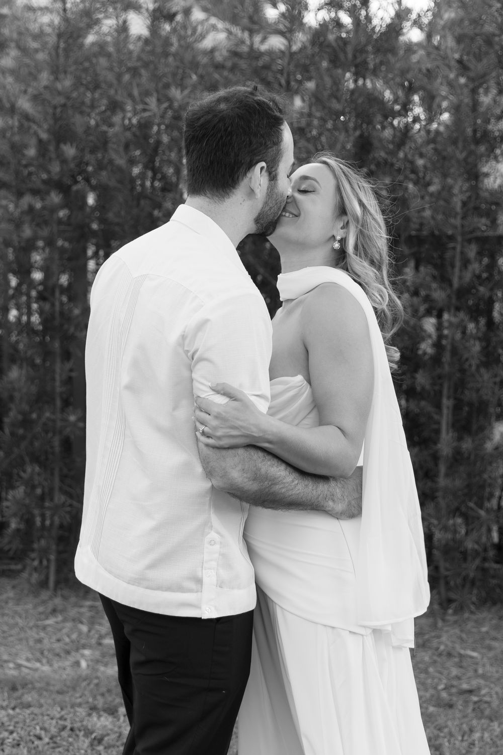 A romantic black and white photo series showing a couple embracing and kissing outdoors in formal attire.