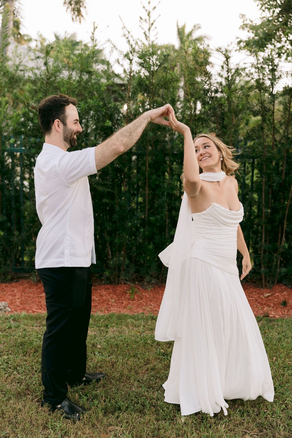 A couple dances together outdoors, with the person in white twirling gracefully against a natural backdrop.