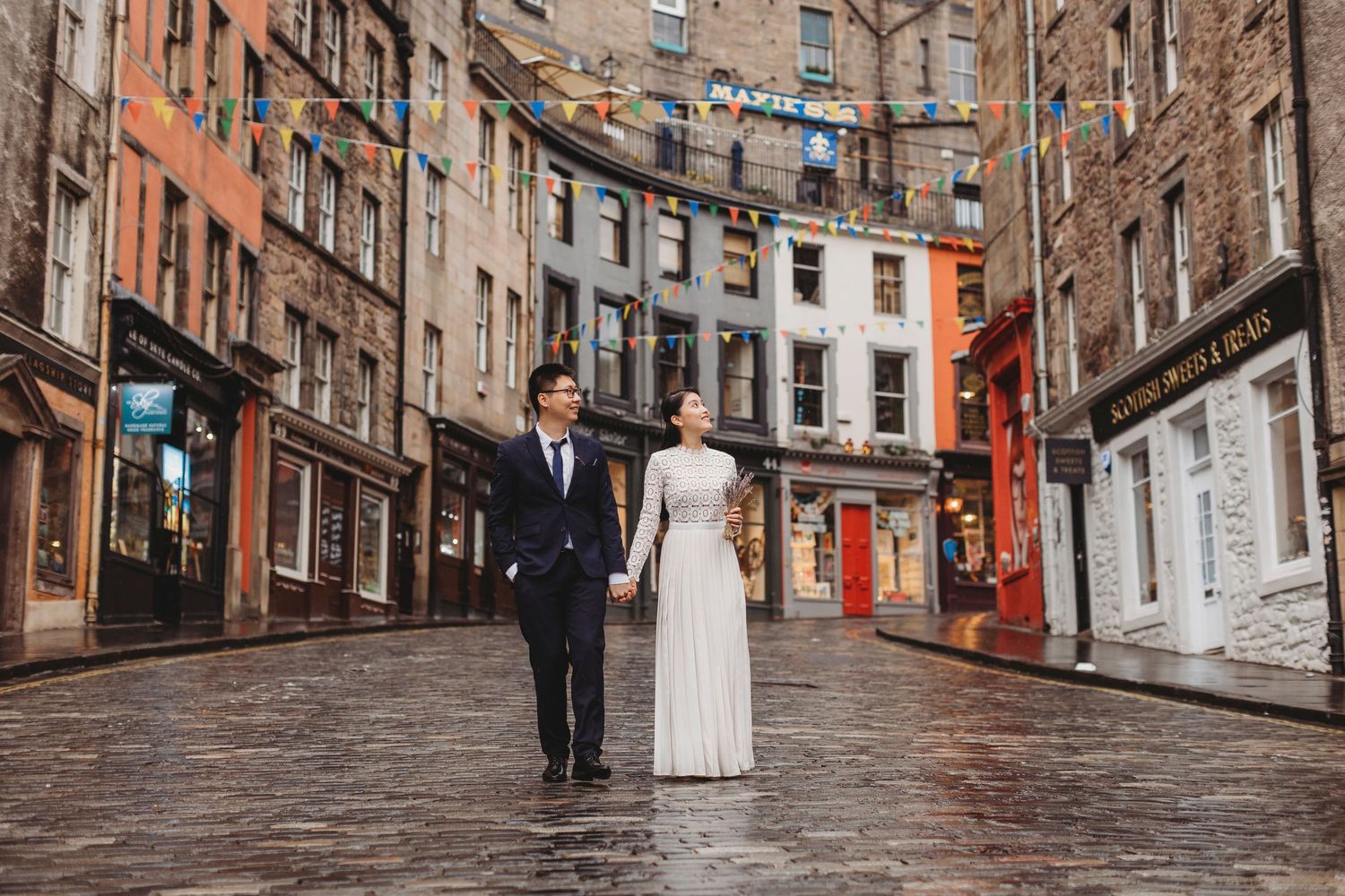 A couple walks down a charming cobblestone street in Edinburgh's historic Old Town on a rainy day.
