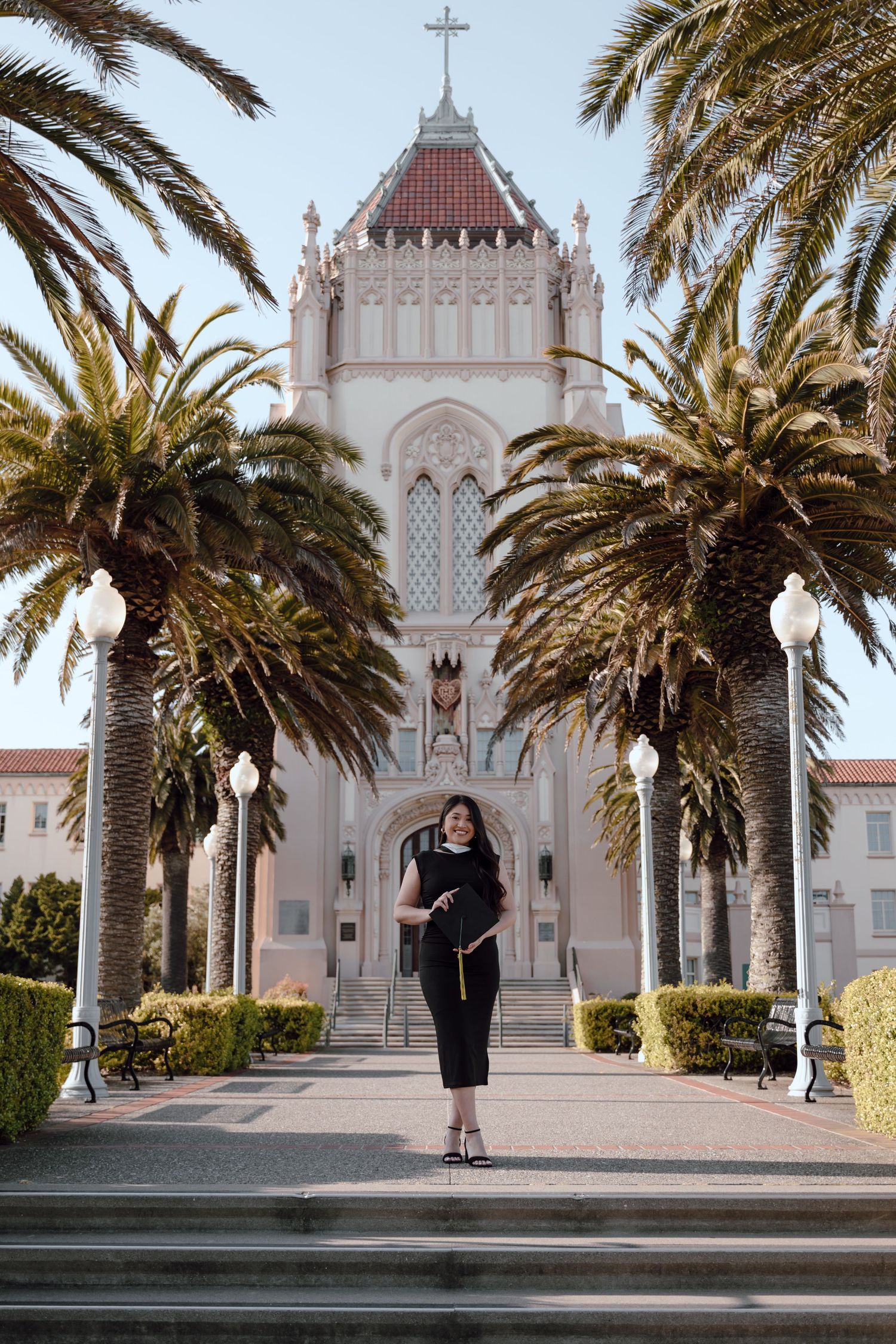 Graduate holds cap and poses in front of Lone Mountain at the University of San Francisco. By Bay Area Graduation Photographer.