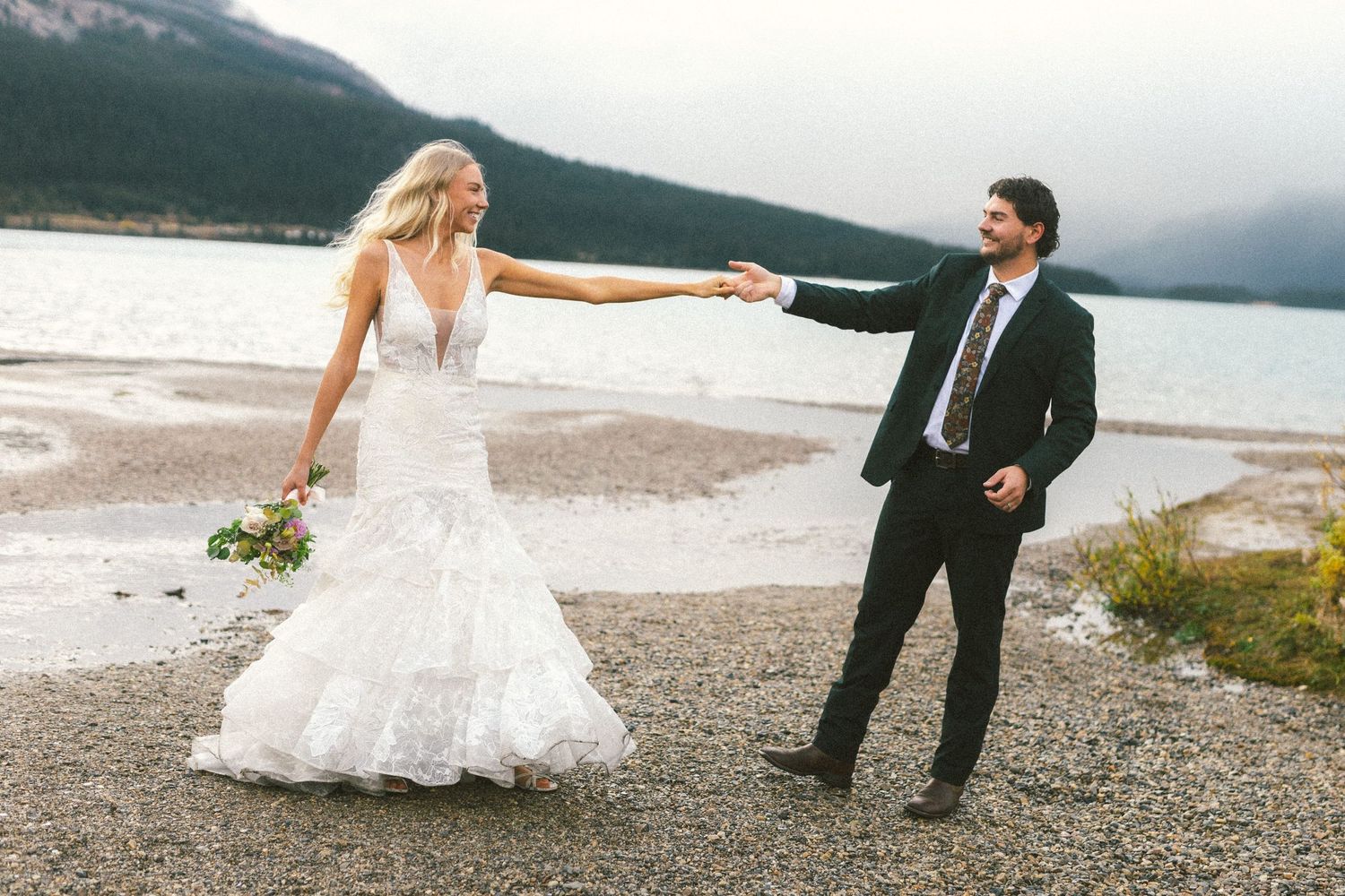 bride and groom spin around and laugh on a lake shore during their elopement