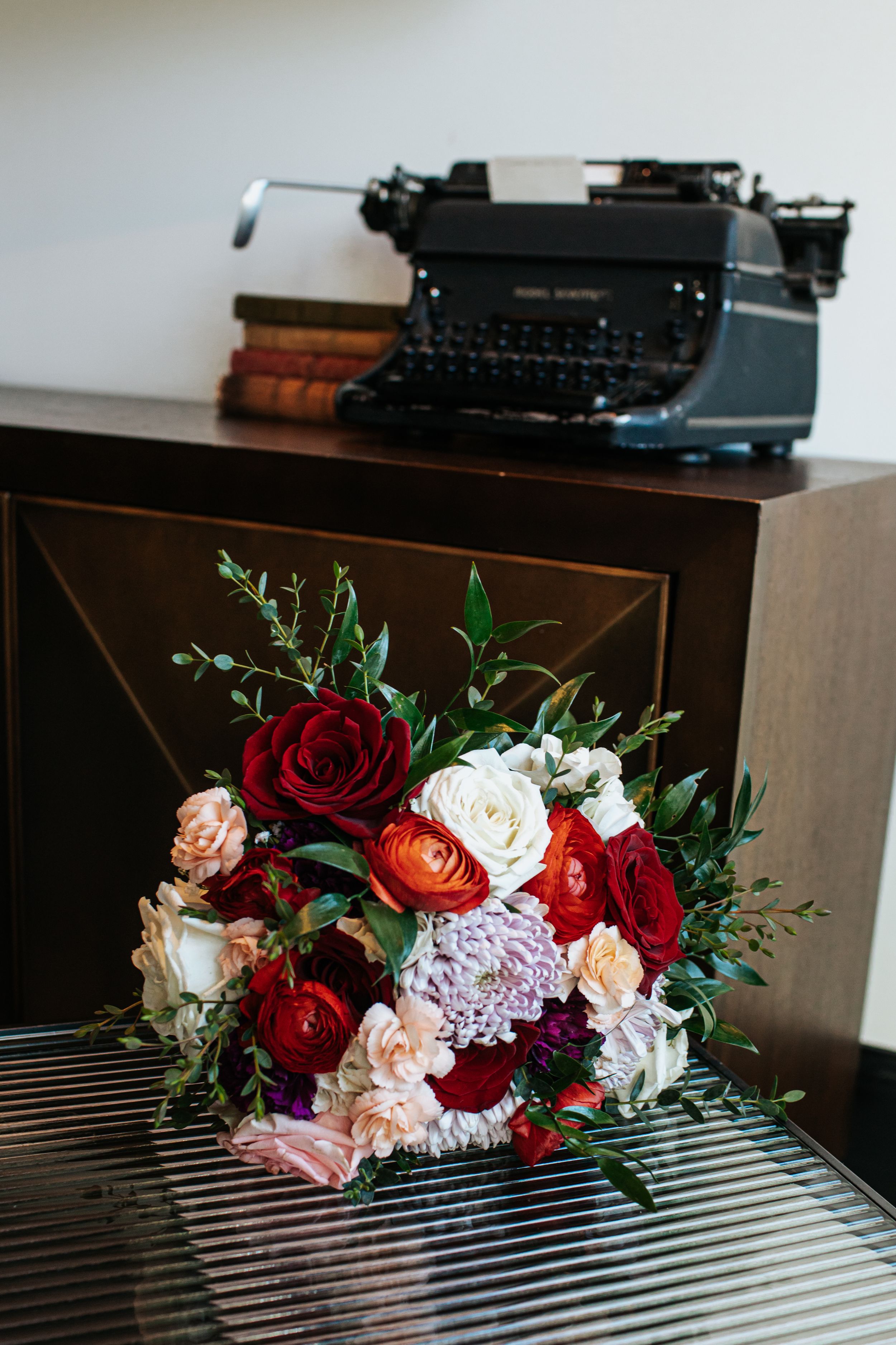 Vintage typewriter with colorful fresh flower arrangements featuring roses and greenery displayed on a wooden surface.