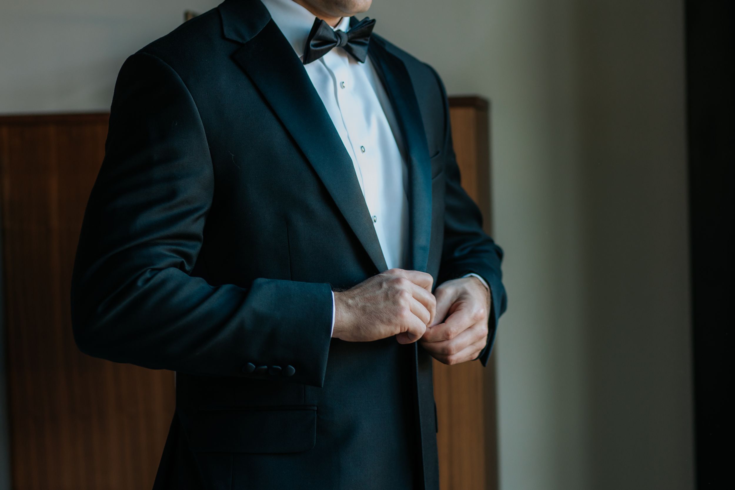Close-up view of a formal black tuxedo jacket with bow tie being adjusted during preparation.
