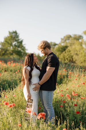 A romantic couple embraces in a sunset-lit meadow filled with vibrant red poppies and wild grass.