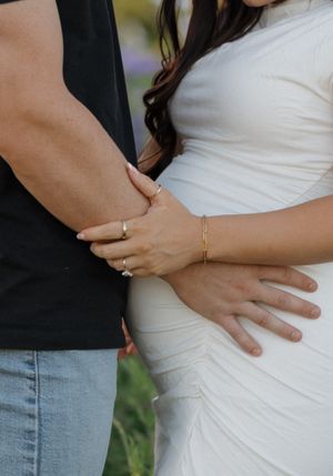 Close-up view of hands wearing delicate jewelry embracing against a white dress and casual attire.
