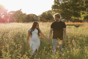 A couple walking together through a sunlit meadow filled with wildflowers during golden hour.