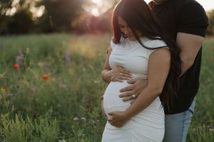 Tender maternity photo with couple embracing in field during golden sunset with wildflowers in background.