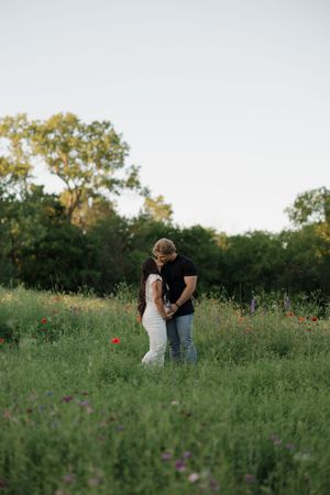 Couple standing together in a wildflower meadow at sunset surrounded by green grass and trees in the background.