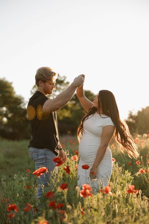A couple dancing together in a poppy field at sunset with beautiful lens flares.