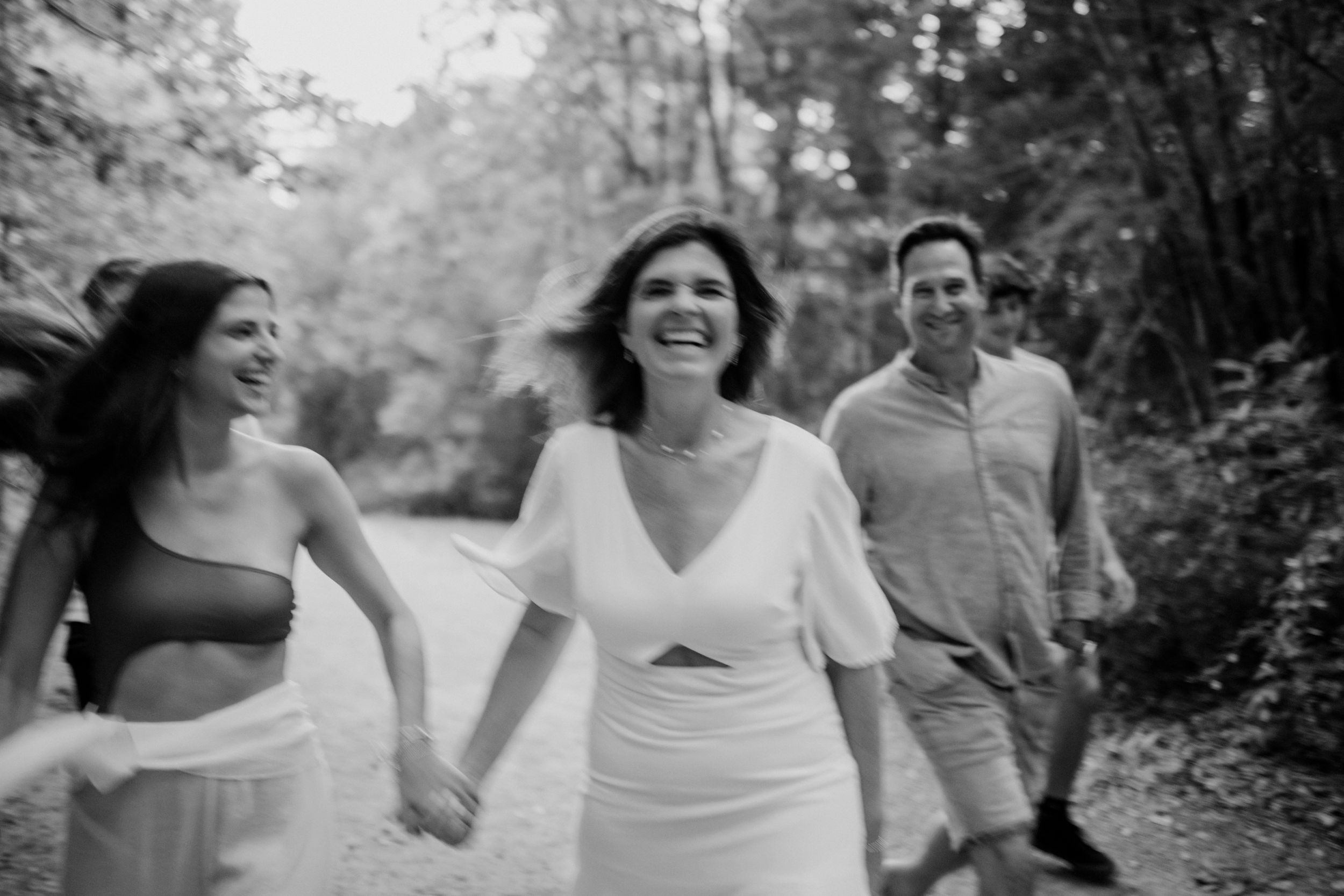 Three people walking together down a wooded path in black and white, laughing and smiling on a sunny day.