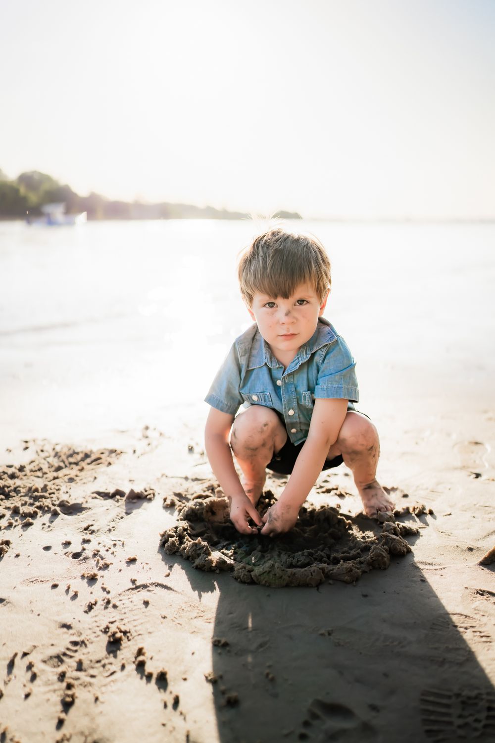 Young child plays in the sand on a bright sunny beach, crouching down to explore the wet sand.