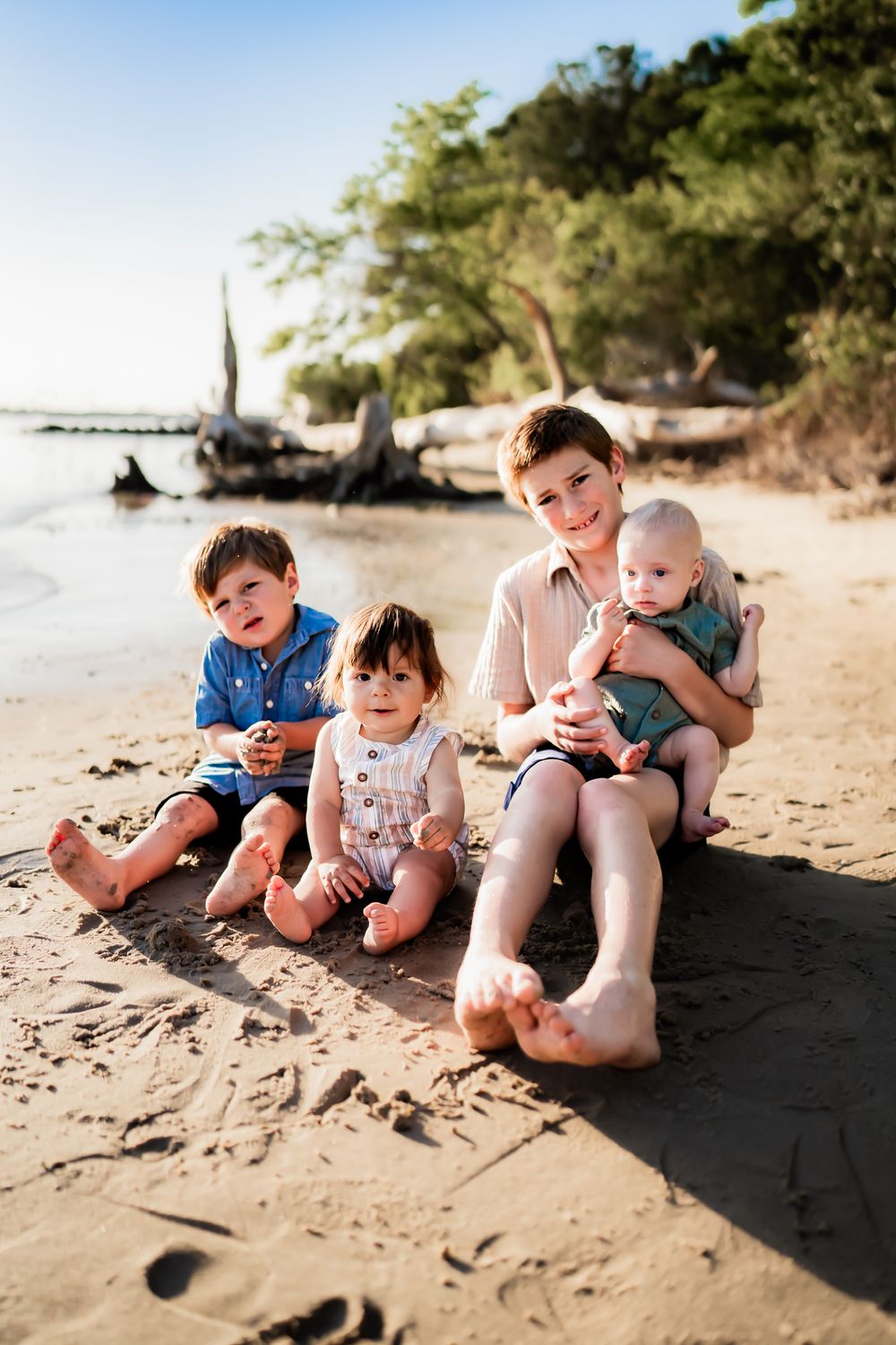 Family enjoying a sunny day at a tropical beach with driftwood and crystal clear waters.