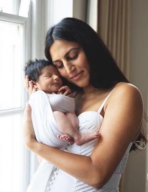 A tender moment between parent and newborn baby beside a bright window in a white room. During a home newborn session in London