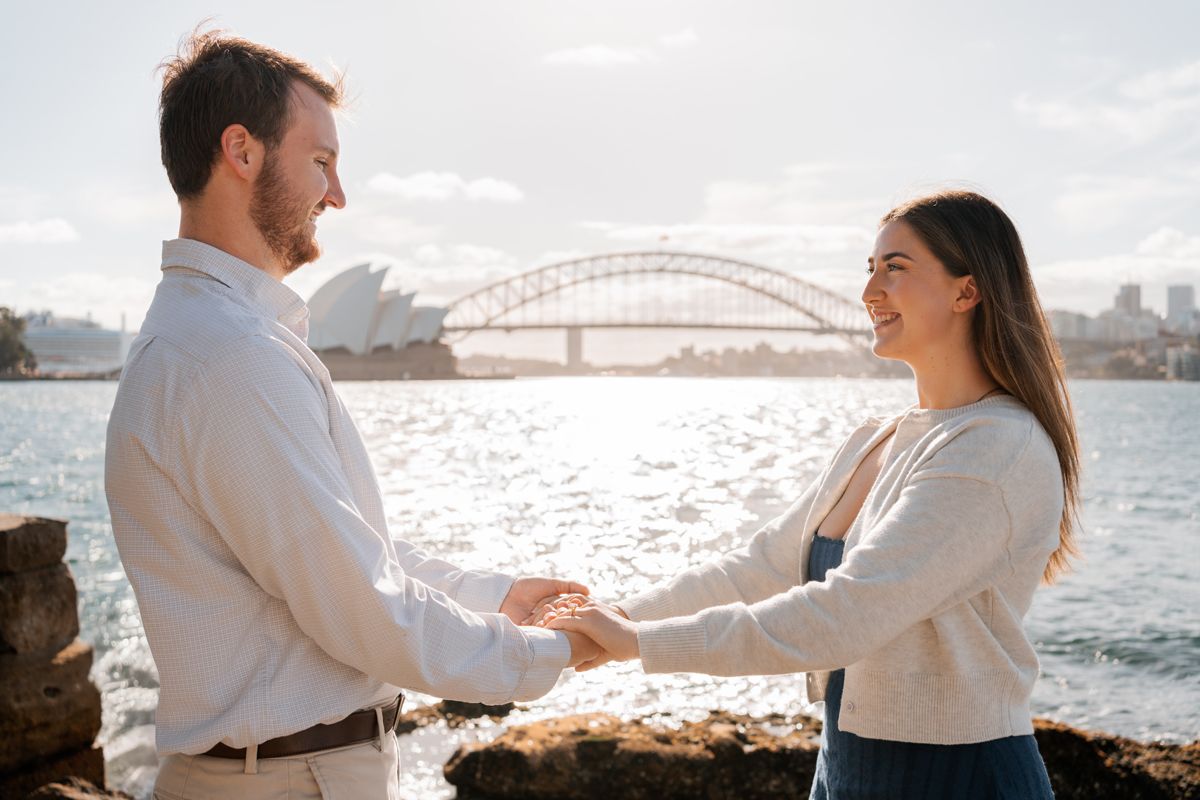 man and woman holding hands looking at each other after a proposal with the opera house and the harbour bridge in the background