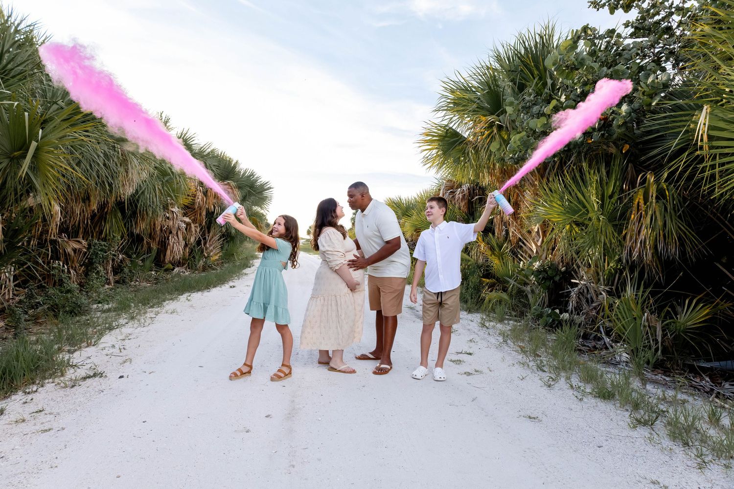 Family walking together on a sandy beach path lined with palm trees.