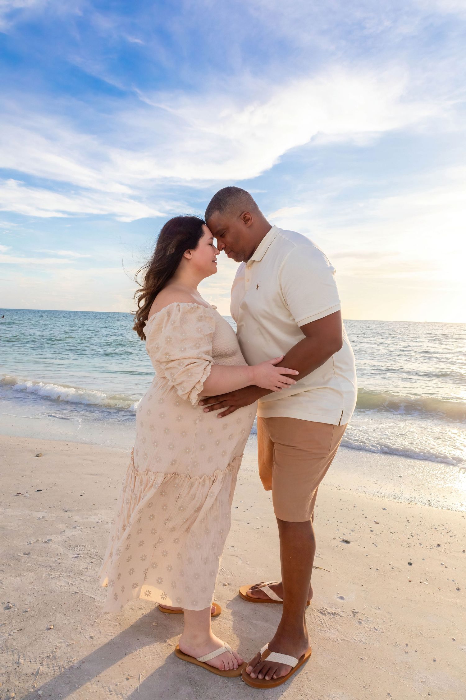 Romantic beach photoshoot with couple dancing in light cream outfits at sunset.