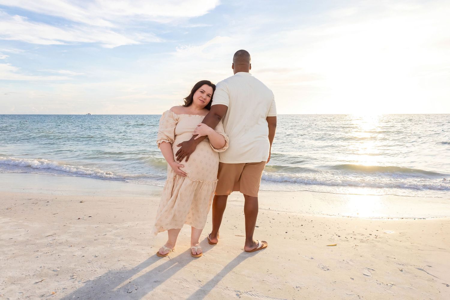 Couple holding hands while walking along shoreline during golden hour.