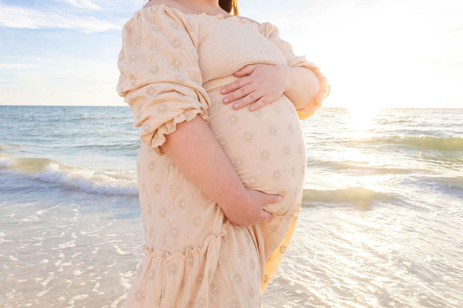 Maternity beach photos with flowing cream dress during golden hour sunset.