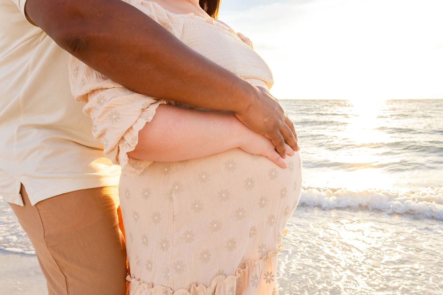 Close-up of maternity pose on beach with couple's hands on baby bump.