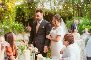 Wedding couple interacts with guests at an outdoor reception with elegant table settings and natural decor.