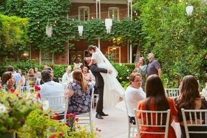 An outdoor garden wedding ceremony with white lanterns and ivy-covered walls creates an intimate atmosphere in a courtyard setting.