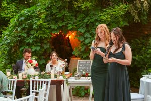 Two people giving speeches at an outdoor garden wedding reception with string lights.