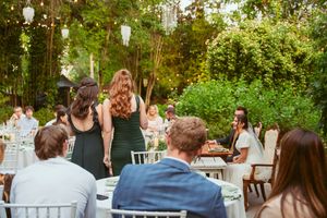Wedding guests enjoying dinner at an outdoor garden reception with white chairs and tables.