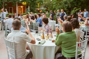 Guests seated at round tables with white linens during an outdoor wedding reception.